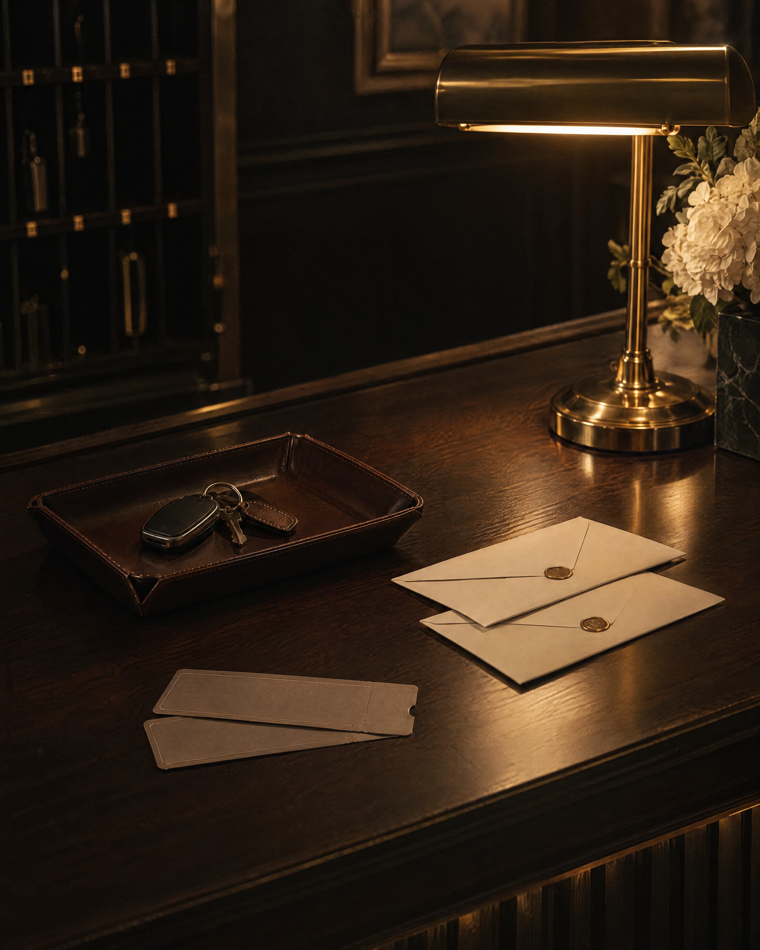 A concierge desk under a brass lamp: a car key in a leather tray, sealed envelopes, two tickets.